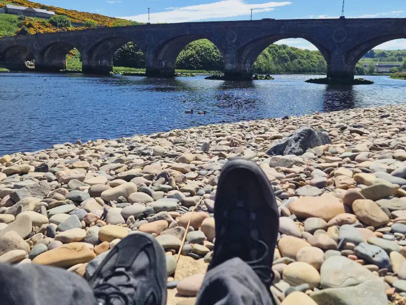 Hiking boots on the pebble beach in front of the old bridge