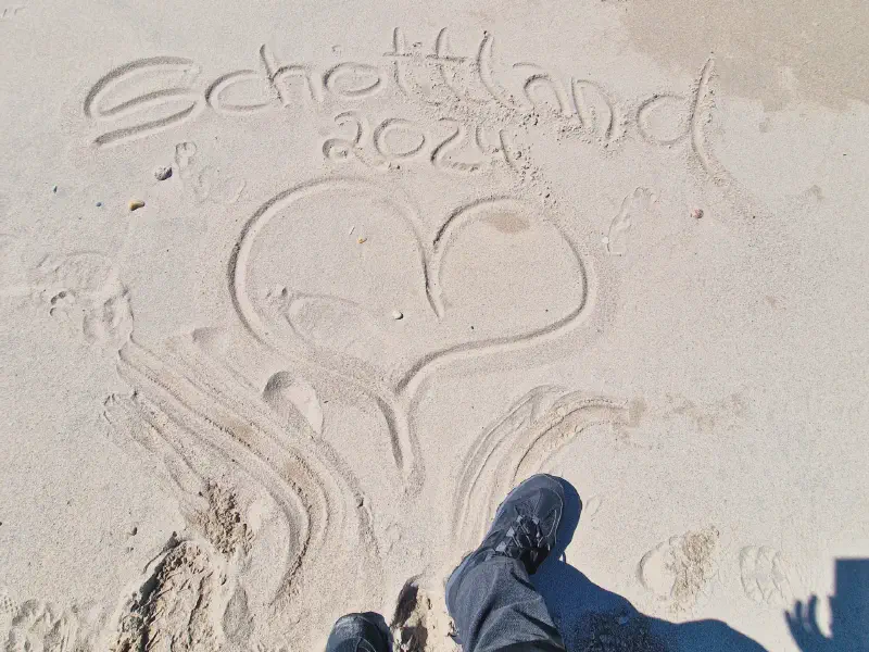 Scotland 2024 written in the sand next to our hiking boots