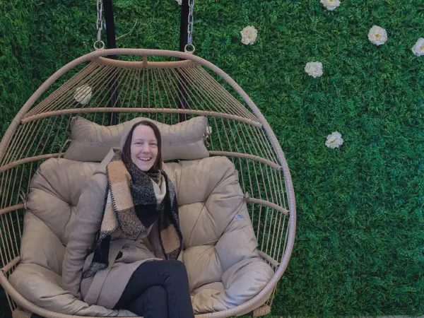 Gina in a comfortable hanging chair in front of the green wall